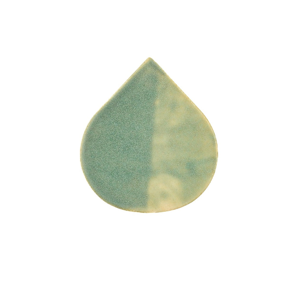 Teardrop-shaped ceramic tile with green and beige pattern on a white background