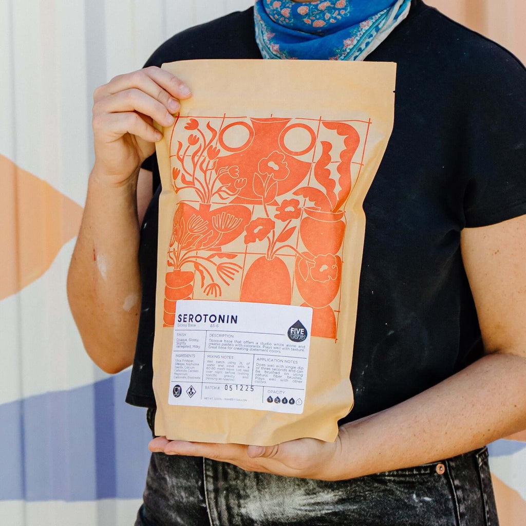 Person holding a package with a colorful design against a geometric-patterned wall.