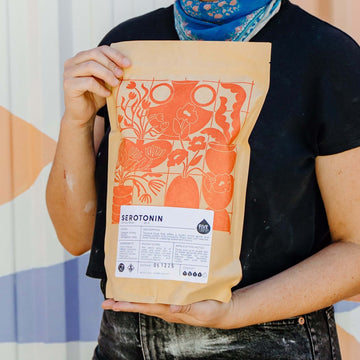 Person holding a package with a colorful design against a geometric-patterned wall.